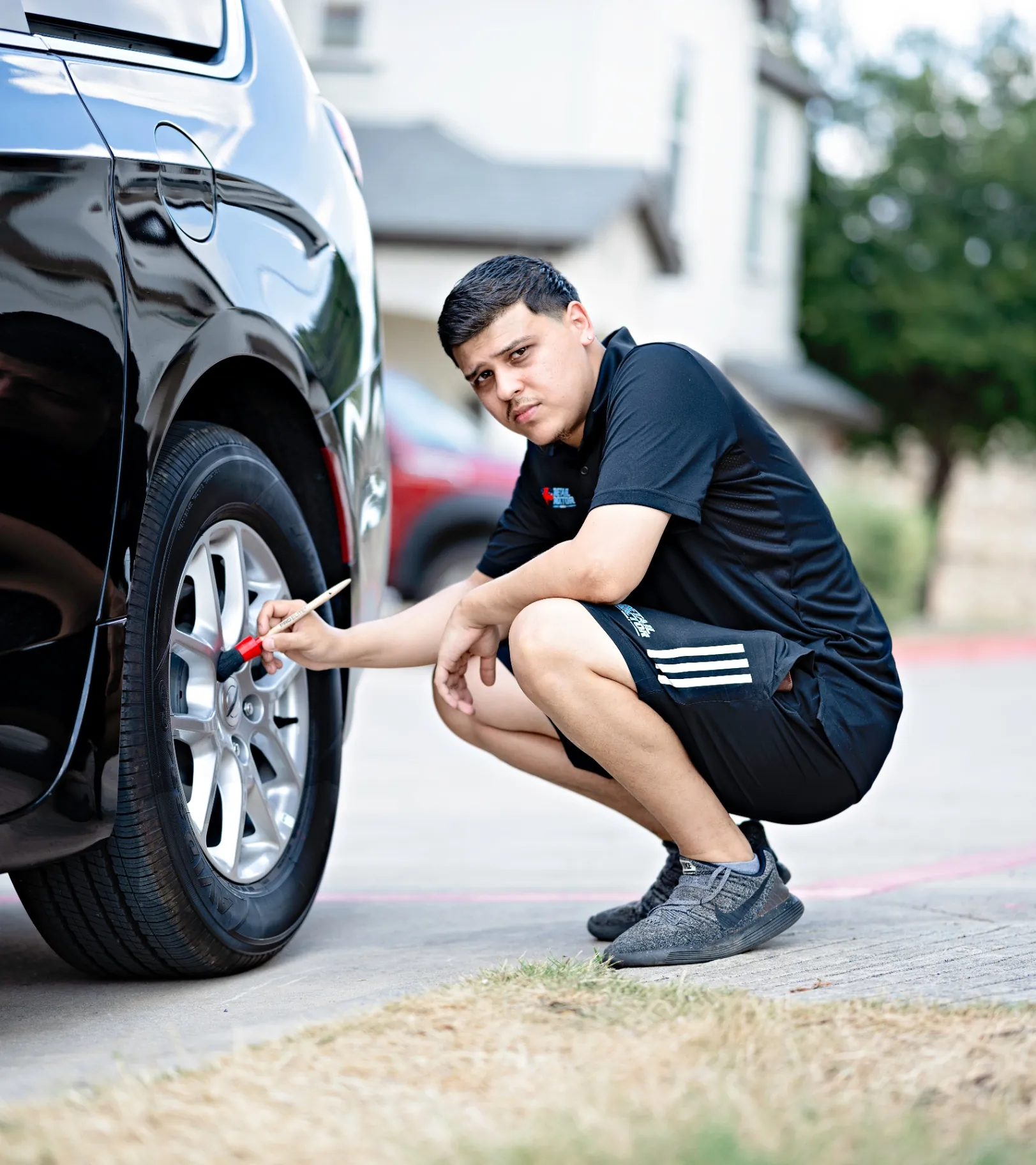 Eric crouched on a driveway, detailing a wheel and tire with a brush